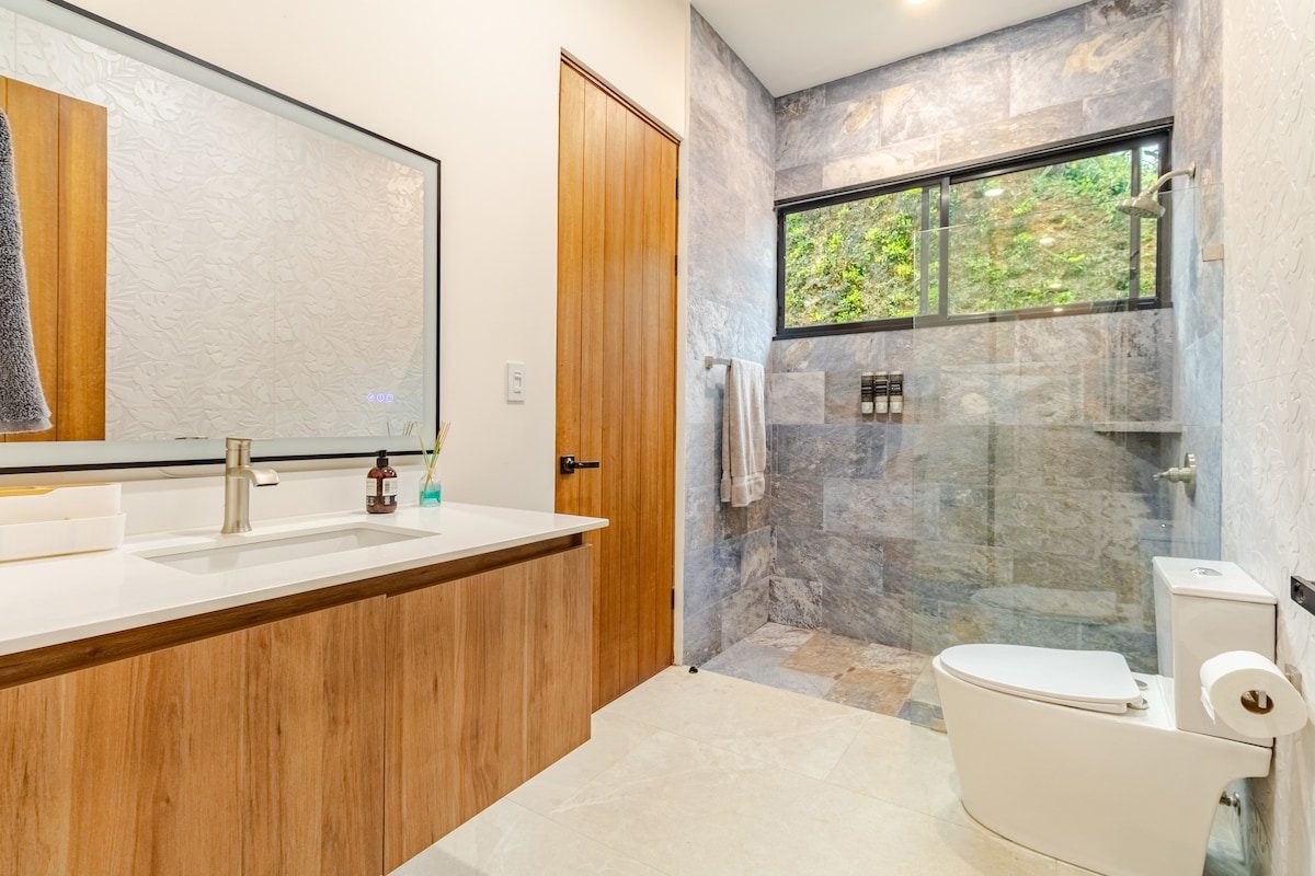 Bathroom with a stone shower and a jungle window